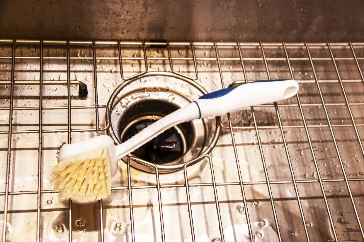 Wet stainless steel sink with garbage disposal and wire rack with scrub brush laying on it