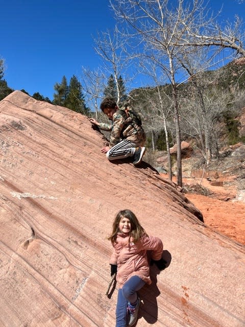 A boy and a girl climbing and posing on a large red rock formation in Zion National Park.