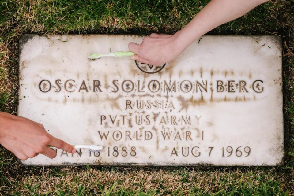 Hands clean a grave with toothbrushes