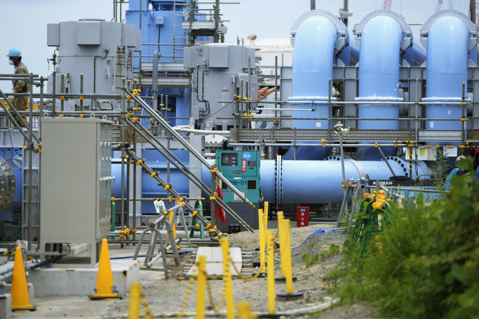 A worker, upper left, walks by a blue pipeline to transport seawater, part of the facility for the release of treated radioactive water to sea from the Fukushima Daiichi nuclear power plant, operated by Tokyo Electric Power Company Holdings, also known as TEPCO, in Futaba town, northeastern Japan, Friday, July 14, 2023. (AP Photo/Hiro Komae)