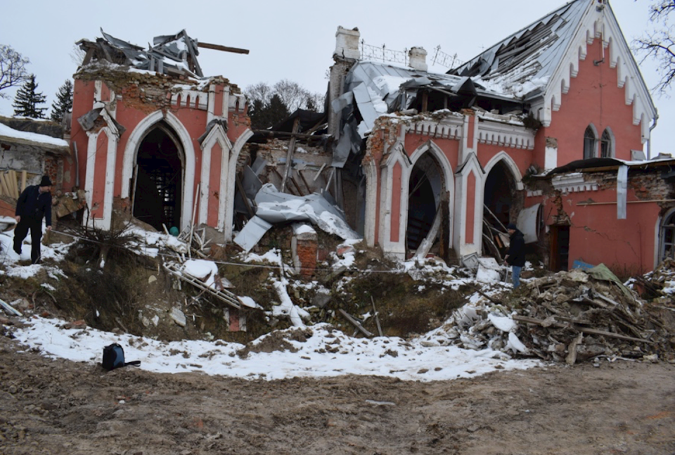 A man looks through rubble near a destroyed pink building.