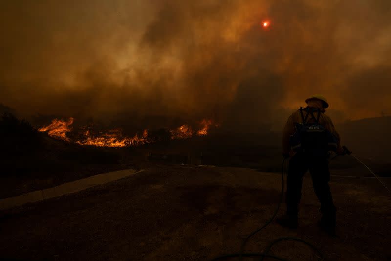 A firefighter uses a homeowners garden hose to help battle the Silverado Fire, a wind driven wildfire near Irvine, California