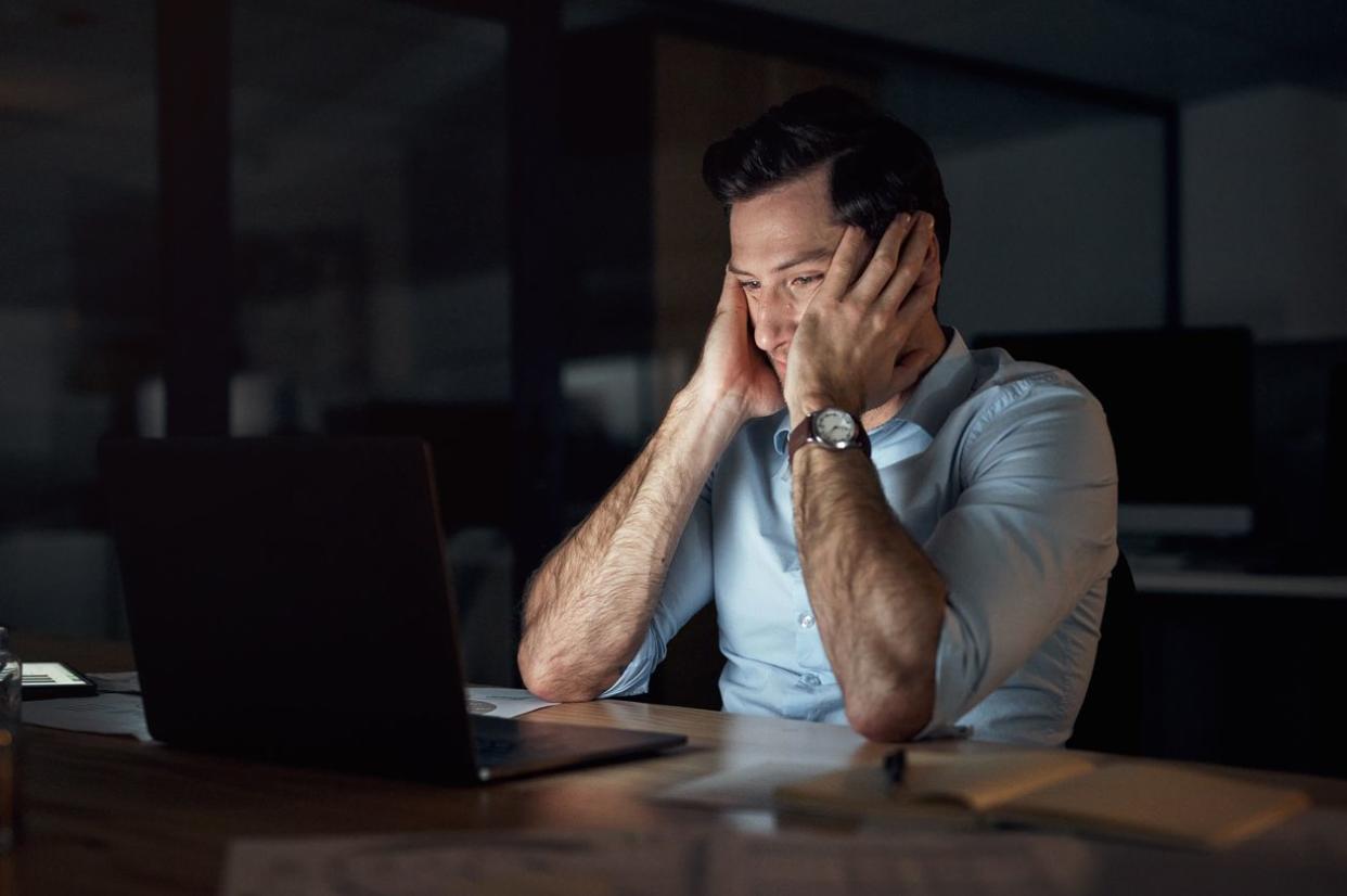 An angry man sitting at his work desk while looking burned out.