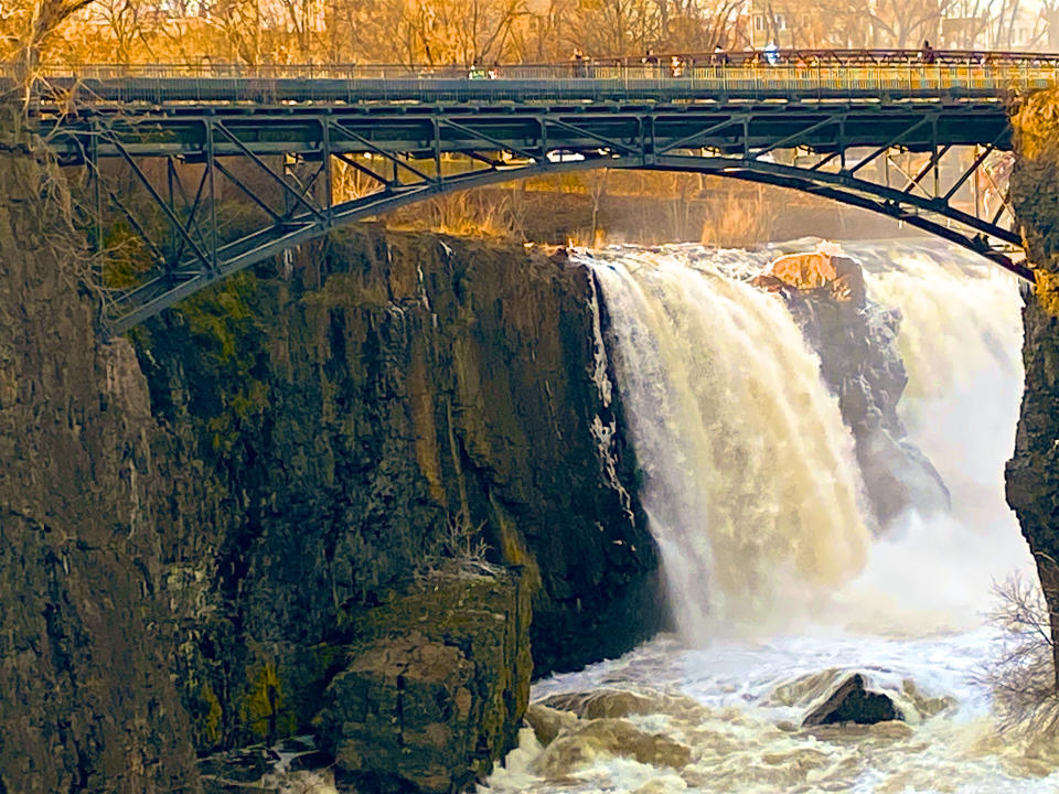 A waterfall thunders down into a river below, while a charming bridge lets visitors view from above.