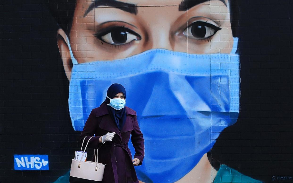 A woman wearing a face mask walks past a piece of street art depicting an NHS worker  - Getty