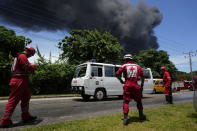 members of the Cuban Red Cross standby as a huge plume of smoke rises from the Matanzas Supertanker Base, as firefighters work to quell a blaze which began during a thunderstorm the night before, in Matazanas, Cuba, Saturday, Aug. 6, 2022. Cuban authorities say lightning struck a crude oil storage tank at the base, causing a fire that led to four explosions which injured more than 50 people. (AP Photo/Ramon Espinosa)