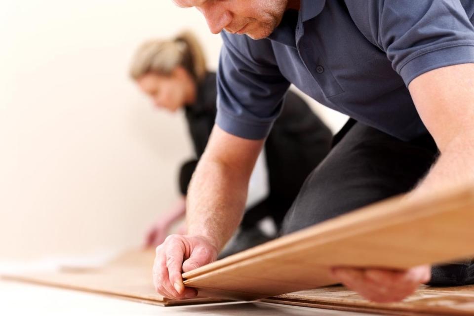 A man fits a wooden plank on a floor. 