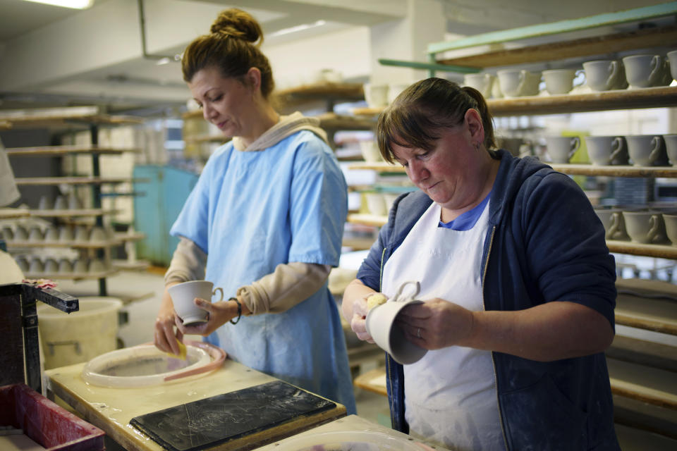 Cups are wiped clear of excess glaze, at the Duchess China 1888 factory, in Stoke-on-Trent, England, Thursday, March 30, 2023. With just five weeks to go until King Charles III’s coronation, an historic pottery is busy producing “God Save The King” commemorative china plates and mugs to mark the occasion. (AP Photo/Jon Super)