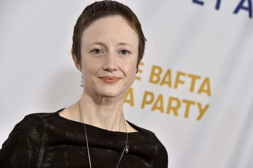 A woman with short hair in a black dress and a long necklace