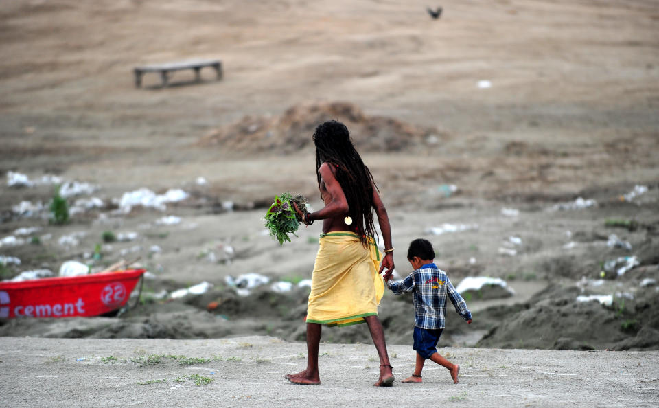 An Indian Hindu Sadhu walks with his adopted child, Bajrangi, on the banks of the Sangam, on father's day in Allahabad on June 16, 2013.  AFP PHOTO / SANJAY KANOJIA        (Photo credit should read Sanjay Kanojia/AFP/Getty Images)