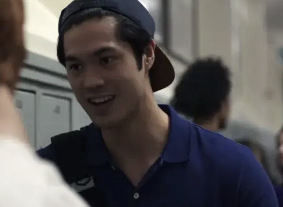 Reggie with backward baseball cap talking to another person in a hallway