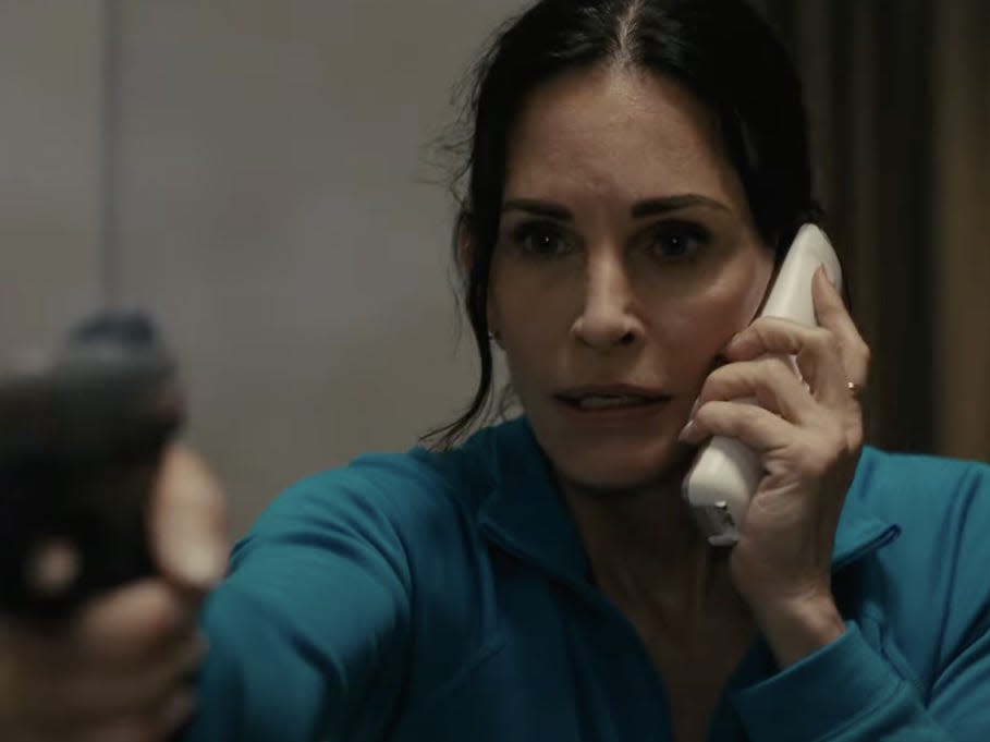 Courtney Cox as Gale Weathers holding a gun and a phone.