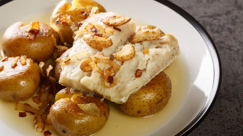 Boiled cod and small potatoes on white plate