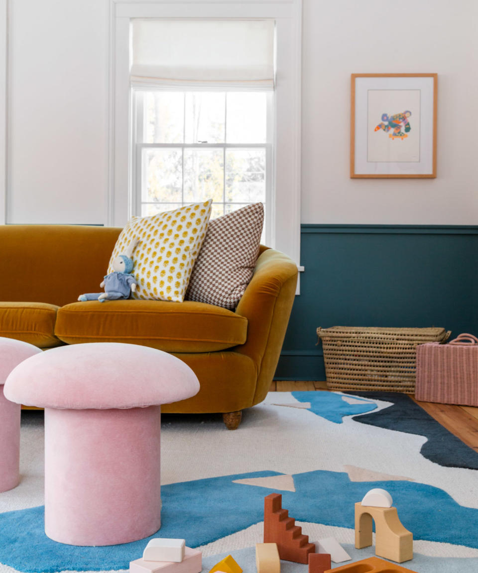 playroom with dark blue lower wall,  gold velvet sofa, pink stools, blue, white and pink patterned rug