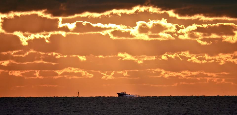 A boat speeds through sunset as seen  from Chapoquoit Beach in West Falmouth.