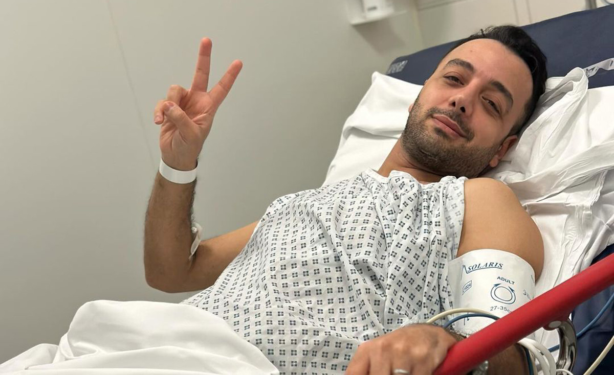 Pouria Zeraati smiling and holding up the peace sign in his hospital bed