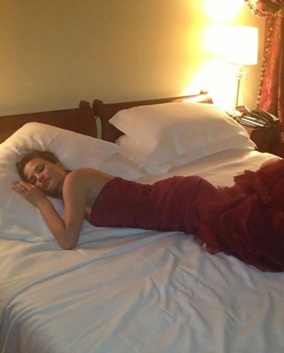 Chrissy Teigen laying on a bed in her crimson wedding gown