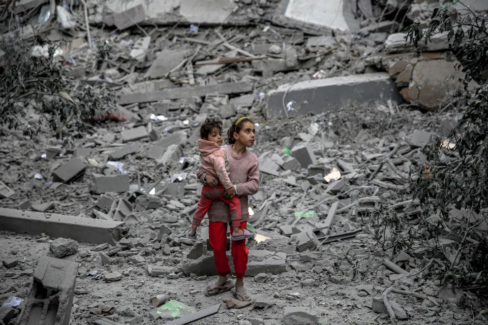 A Palestinian girl carries a child through the rubble of houses destroyed by Israeli bombardment in Gaza City on March 3, 2024.