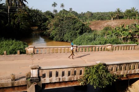 A woman crosses a bridge over a river polluted by gold mining waste in Nsuaem district