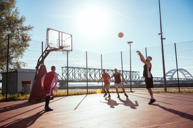 Five men play basketball outdoors.