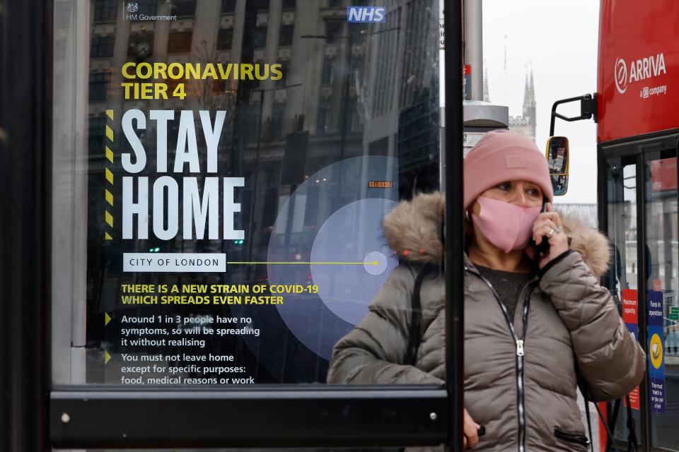 A passenger wearing a mask because of the coronavirus pandemic talks on the telephone waiting at a bus stop with a government message about the coronavirus tier 4 restrictions urging people to stay home in London on December 29, 2020. - England is "back in the eye" of the coronavirus storm, health chiefs warned Tuesday, with as many patients in hospital as during the initial peak in April. (Photo by Tolga Akmen / AFP) (Photo by TOLGA AKMEN/AFP via Getty Images)