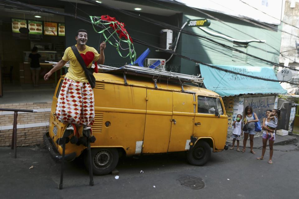 A street artist (L) holding an umbrella fixed with hearts makes a performance as he enters Rocinha slum in Rio de Janeiro March 13, 2014. The artist was giving out hearts to people who passed him, which he says is a symbol of peace. REUTERS/Pilar Olivares (BRAZIL - Tags: SOCIETY)