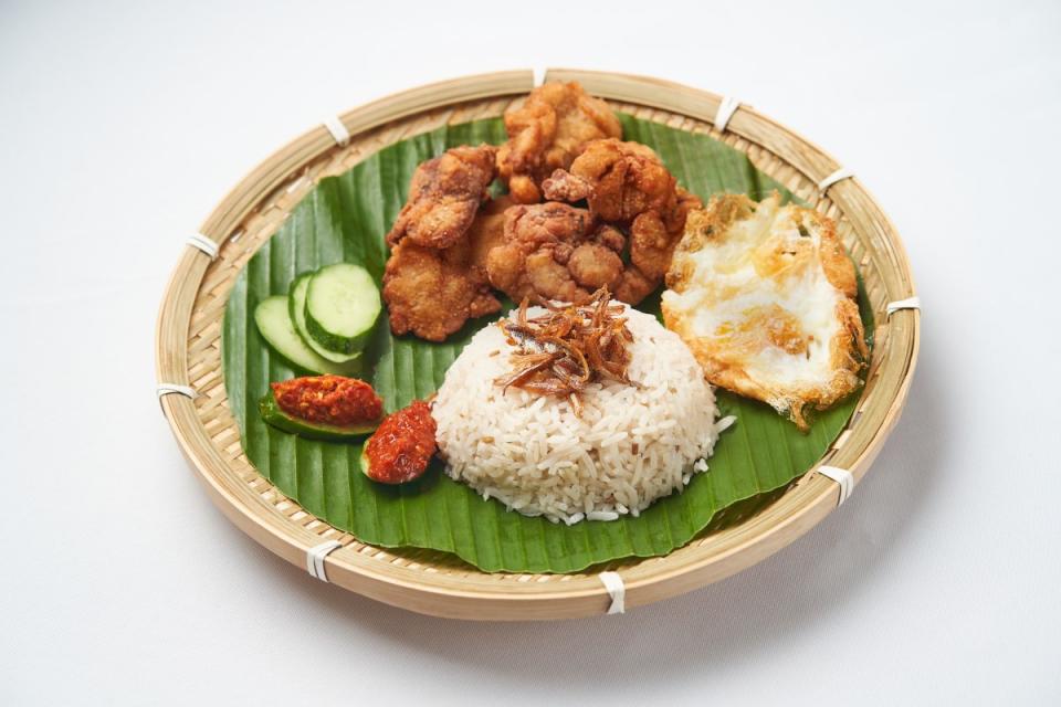 A plate of Nasi Lemak with its ingredients of fried egg, fried chicken, anchovies, cucumber and chilli.