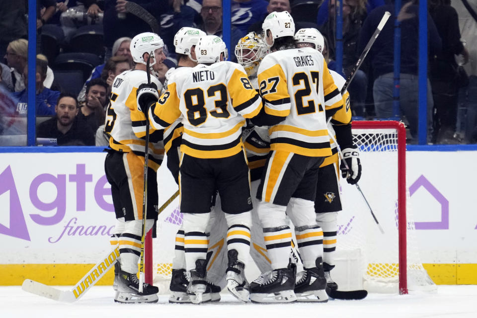 Pittsburgh Penguins goaltender Tristan Jarry is mobbed by teammates, including left wing Matt Nieto (83), and defenseman Ryan Graves (27) after scoring against the Tampa Bay Lightning during the third period of an NHL hockey game Thursday, Nov. 30, 2023, in Tampa, Fla. (AP Photo/Chris O'Meara)