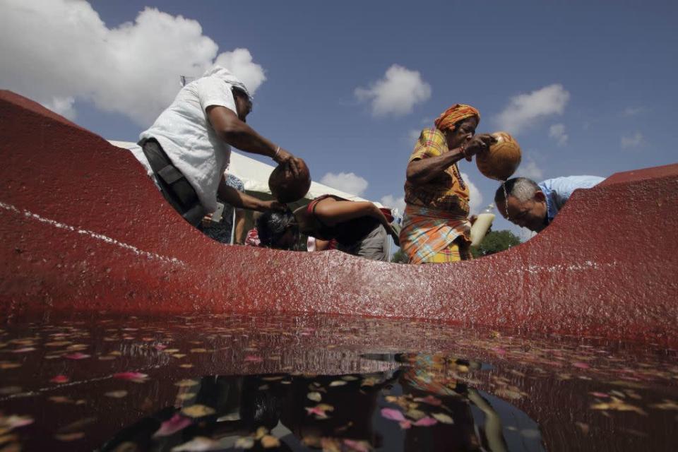 Rita Ravenberg (L) and Elly Purperhart (2nd R) of the National Federation of African-Surinamese pours sacred water containing herbs and flowers on people from all origins during a New Year's Eve ritual at the Independence Square in Paramaribo, Suriname, December 31, 2012. The sacred water is prepared by a spiritual leader in a former sugar cane cooking pot used in the time of slavery to symbolize that bad experiences in the past can be turned into good ones by the people themselves. It is believed that the sacred water will wash away bad spirits and welcome good ones, as well as bring luck, fortune and health for the coming year.