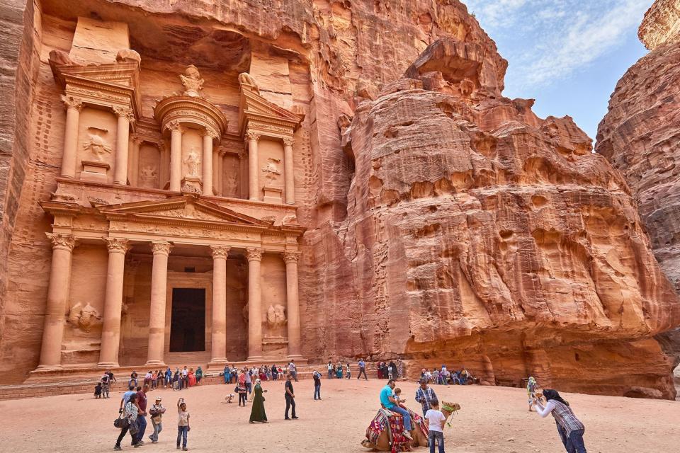 Tourists stand in front of the Treasury in Petra, which is carved into the rock.