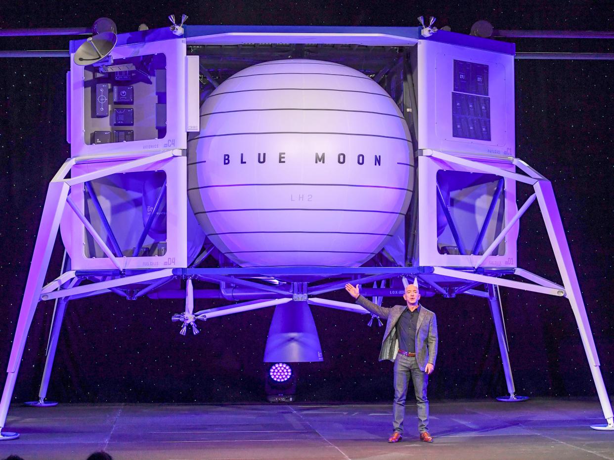 Jeff Bezos gesturing towards a space lander, which looks like an orb with four legs.