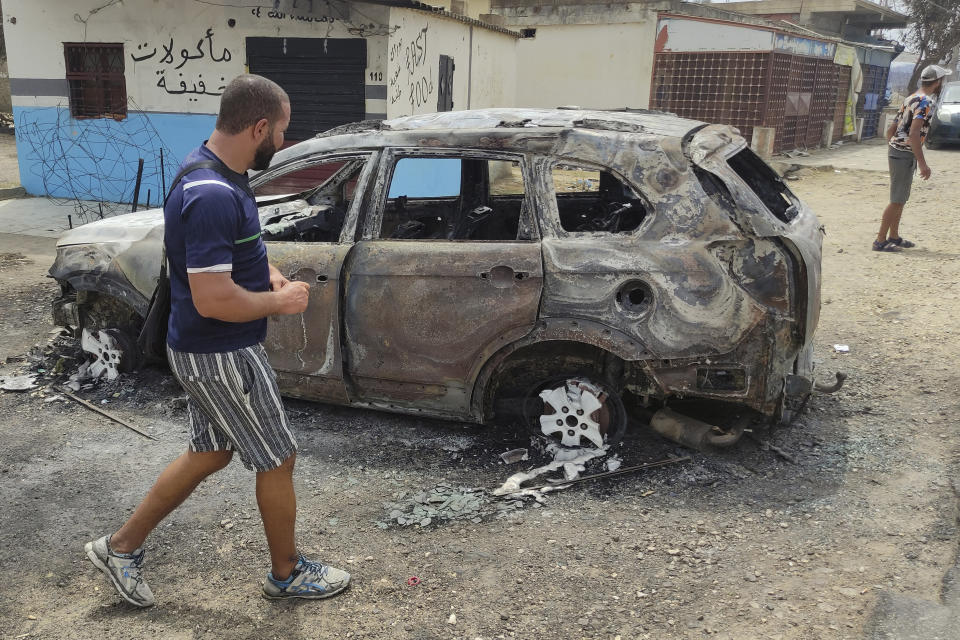 A man walks past a charred car in a village of the region of El Tarf, near the northern Algerian-Tunisian border, Thursday, Aug.18, 2022. Wildfires raging in the forests of eastern Algeria have killed at least 26 people, according to a "provisional report" by the north African country's interior minister. (AP Photo/Mohamed Ali)