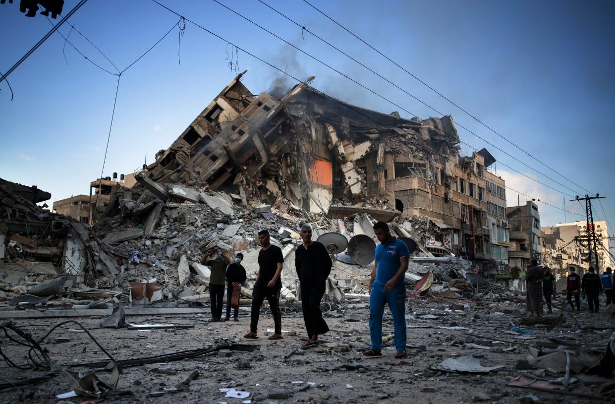Palestinians walk next to the remains of a destroyed 15-story building after being hit by Israeli airstrikes on Gaza City, Thursday, May 13, 2021.