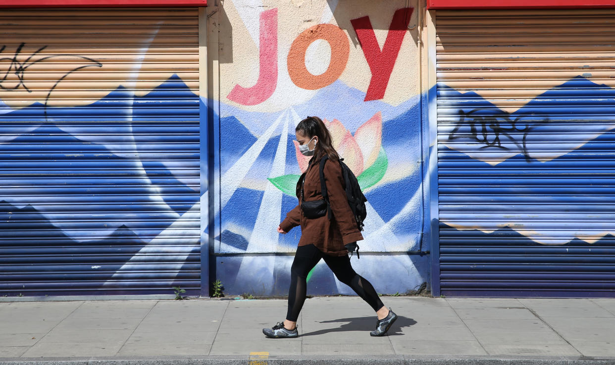 A woman wearing a face mask walks past a graffiti that reads “Joy” in Dalston, Hackney, east London, as the UK continues in lockdown to help curb the spread of the coronavirus. Picture date: Saturday May 2, 2020.