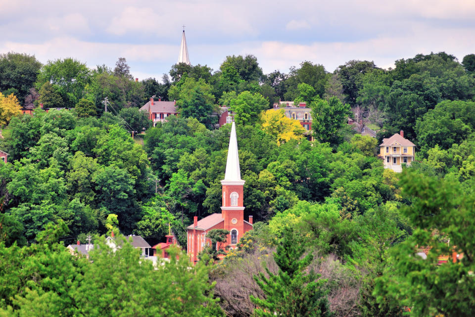 A scenic view of a small town with a prominent church steeple surrounded by green trees and houses in the background