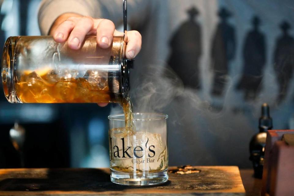 Bartender Cavanaugh Ragone, of Nicholasville, Ky., pours a Smoked Old Fashioned made with a Knob Creek barrel pick mixed with leather and tobacco bitters made in-house along with cocktail bitters, agave nectar, a roasted orange peel, Luxardo cherries, and limestone spring water at Jake’s Cigar Bar in Nicholasville. The cocktail is served in a glass lined with smoke from the wood of the barrel pick.