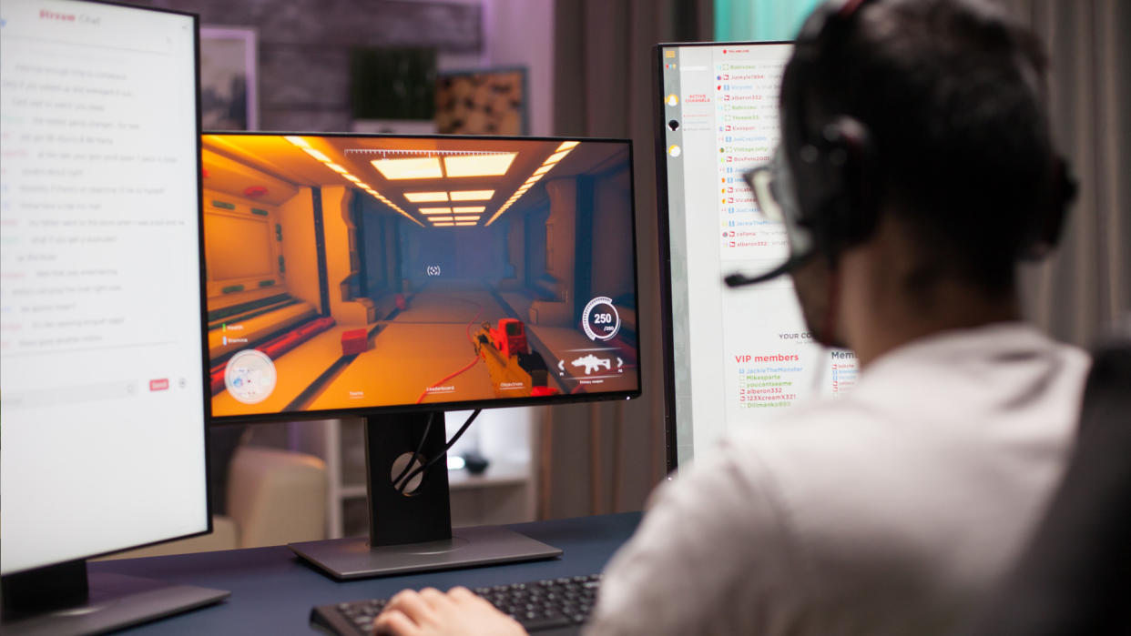  Young man playing shooter competitive game in a dark room wearing headphones. 