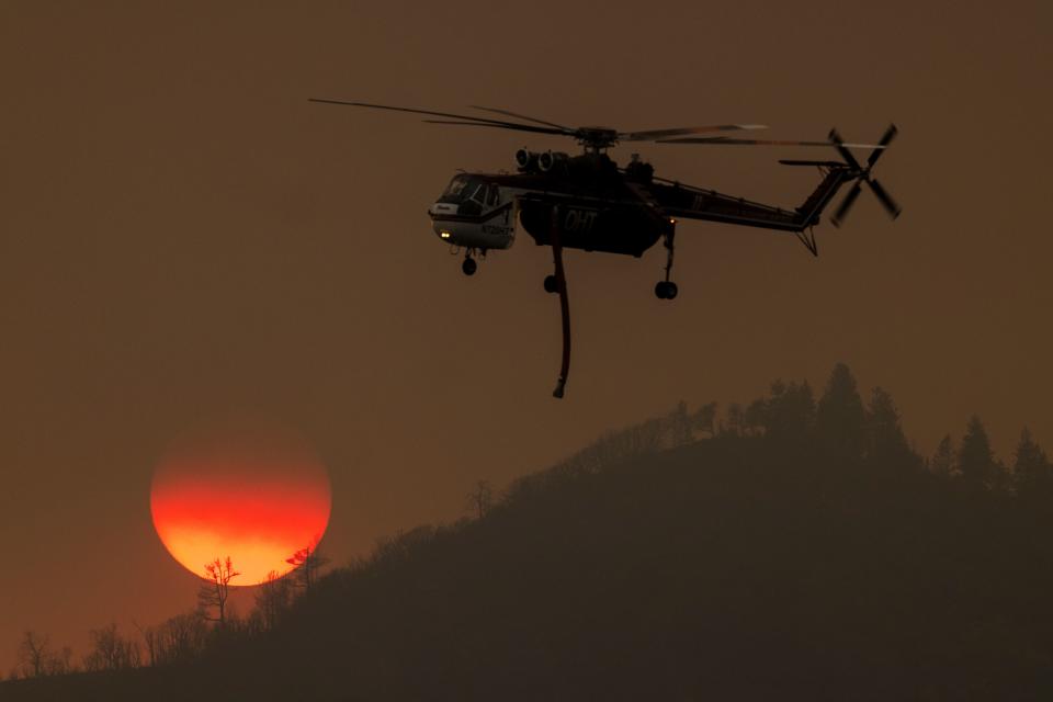 A firefighting helicopter passes the setting sun.