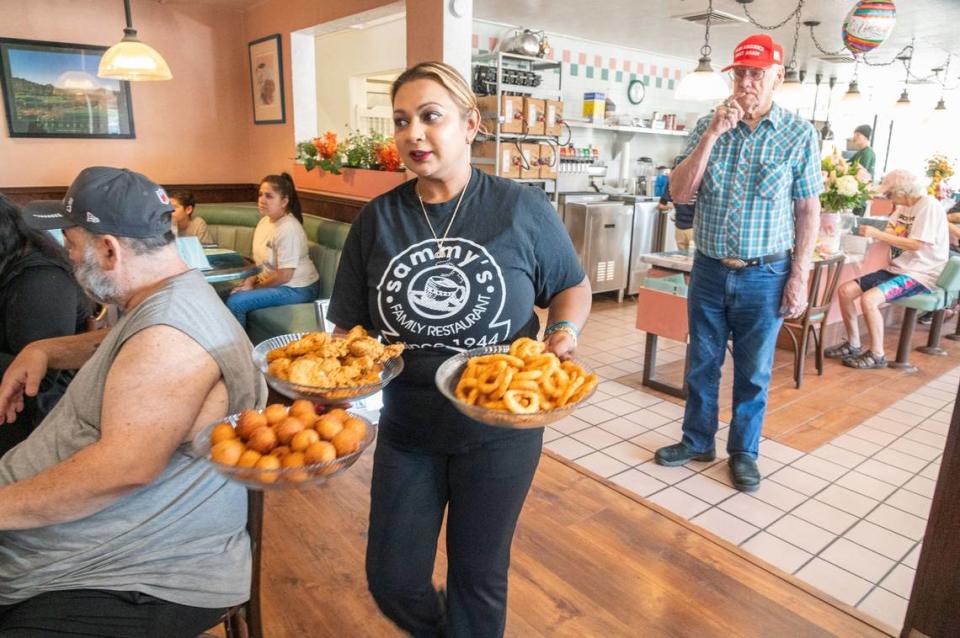 Sammy’s Restaurant owner Naz Begum serves fried foods to attendees during the restaurant’s grand reopening in North Sacramento on Friday. “This district, too, has so much potential, so much life,” Begum said. “And I think more business here will bring more life here.”