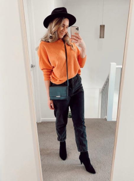 Woman in black jeans, a black hat and orange jumper