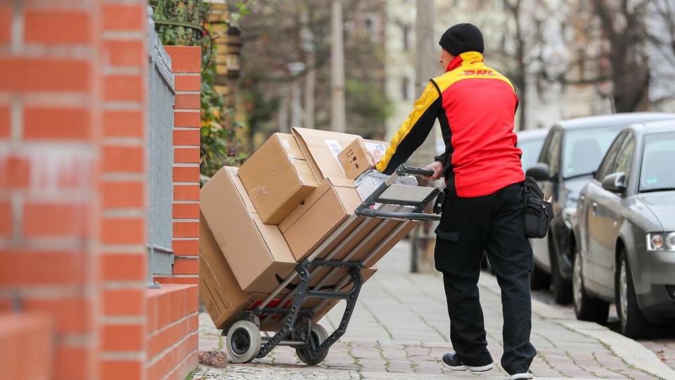 Ein DHL-Paketzusteller geht mit einer Sackkarre voller Pakete zu einem Haus.