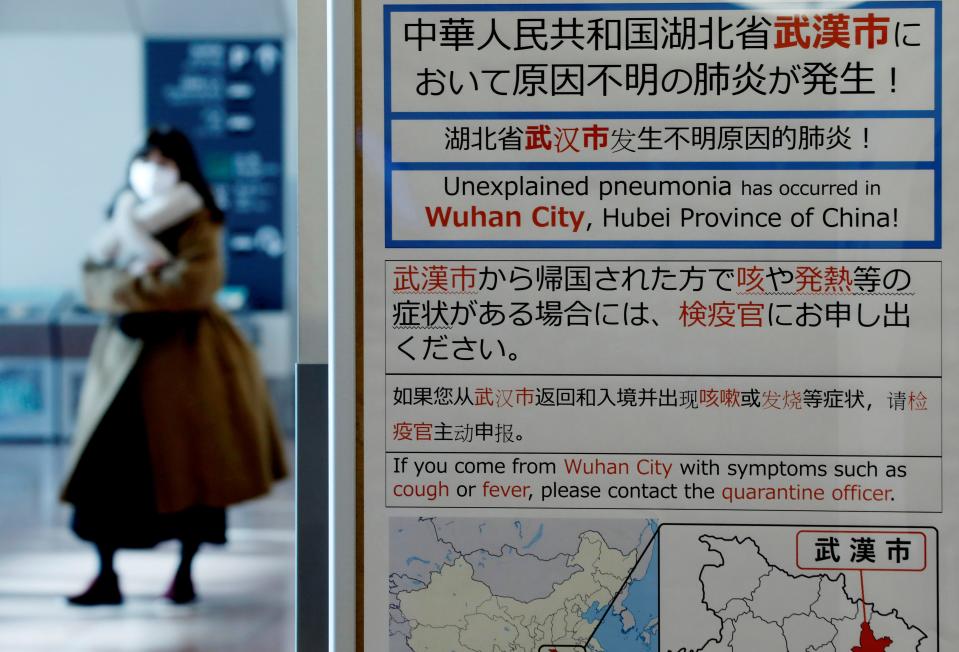 FILE PHOTO: A woman wearing a mask walks past a quarantine notice about the outbreak of coronavirus in Wuhan, China at an arrival hall of Haneda airport in Tokyo, Japan, January 20, 2020. REUTERS/Kim Kyung-Hoon/File Photo