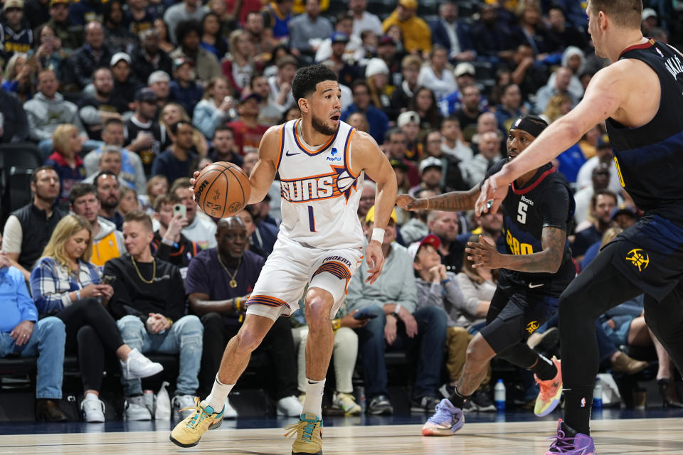 Phoenix Suns guard Devin Booker looks to pass the ball as Denver Nuggets guard Reggie Jackson, back right, and center Nikola Jokic defend during the first half of an NBA basketball game Wednesday, March 27, 2024, in Denver. (AP Photo/David Zalubowski)