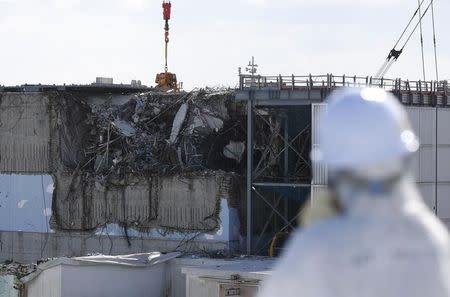 A member of the media, wearing a protective suit and a mask, looks at the No. 3 reactor building at Tokyo Electric Power Co's (TEPCO) tsunami-crippled Fukushima Daiichi nuclear power plant in Okuma town, Fukushima prefecture, Japan February 10, 2016. REUTERS/Toru Hanai/Files