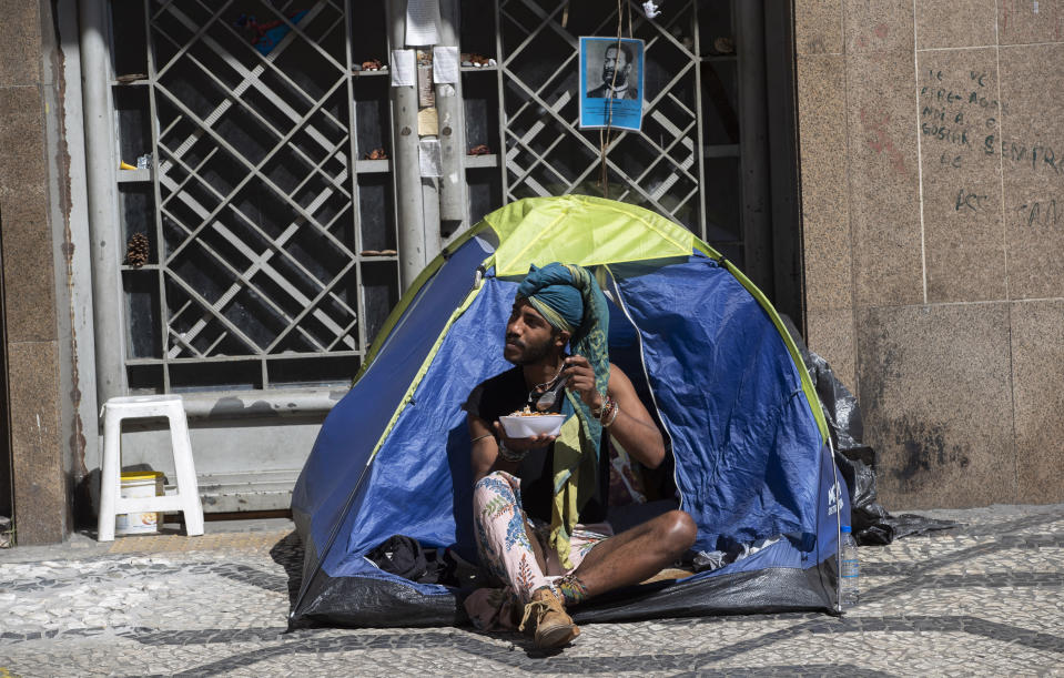 A homeless man eats food given to him by volunteers during a quarantine imposed by the state government to help contain the spread of the new coronavirus in Sao Paulo, Brazil, Monday, April 27, 2020. (AP Photo/Andre Penner)