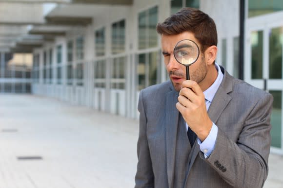 Person in an ill-fitting suit looking through a magnifying glass.