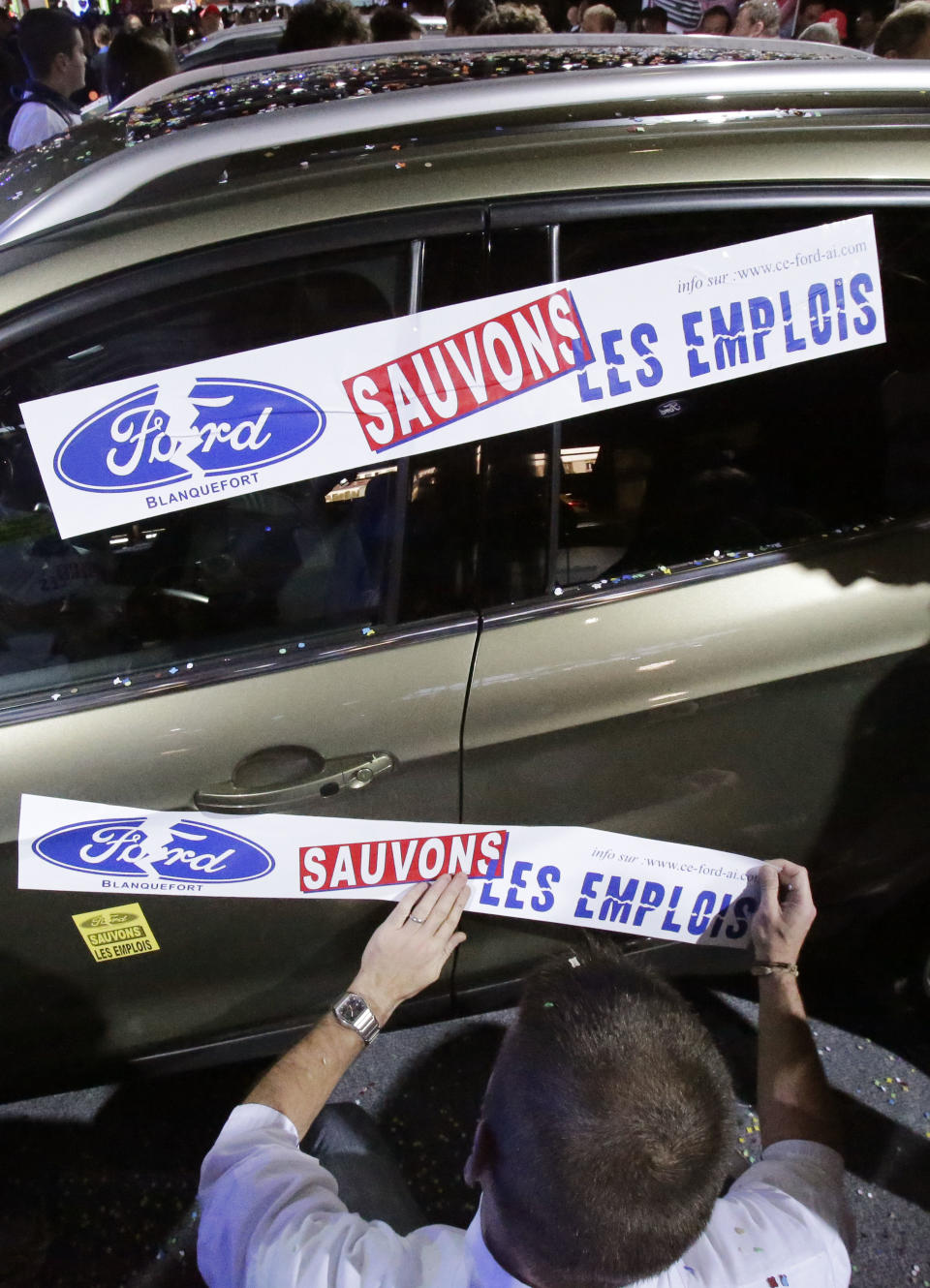 A protestor from a Ford factory in France attaches a giant sticker that reads: "Save the Jobs" to a Ford Mondeo, during a protest against factory policy at the Paris Auto Show, France, Saturday, Sept. 29, 2012. The workers swarmed the Paris Auto Show with giant stickers, plastering about 20 cars around the hall to protest lost jobs in the automotive industry. (AP Photo/Michel Euler)