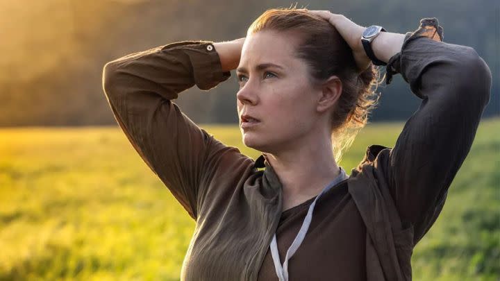 Amy Adams as Louise Banks with her hands on her head standing in a field looking up in Arrival.