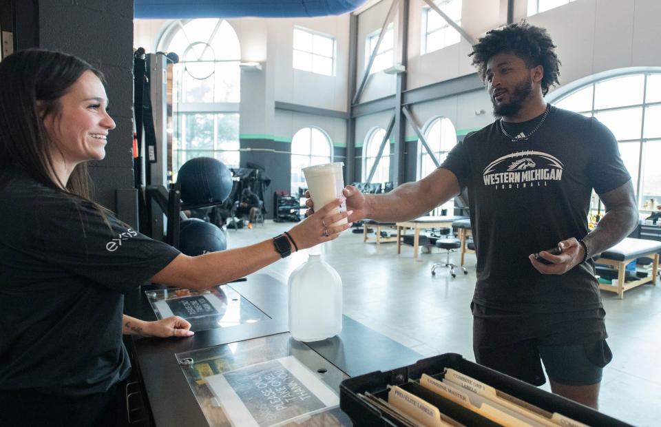 Nutritian intern Jess Collette, left, hands a recovery shake to former Western Michigan University football player Marshawn Kneeland as he works out at the Exos training facility at the Andrews Institute in Gulf Breeze on Friday, Feb. 17, 2024. Kneeland and other players are preparing for the upcoming NFL Scouting Combine.