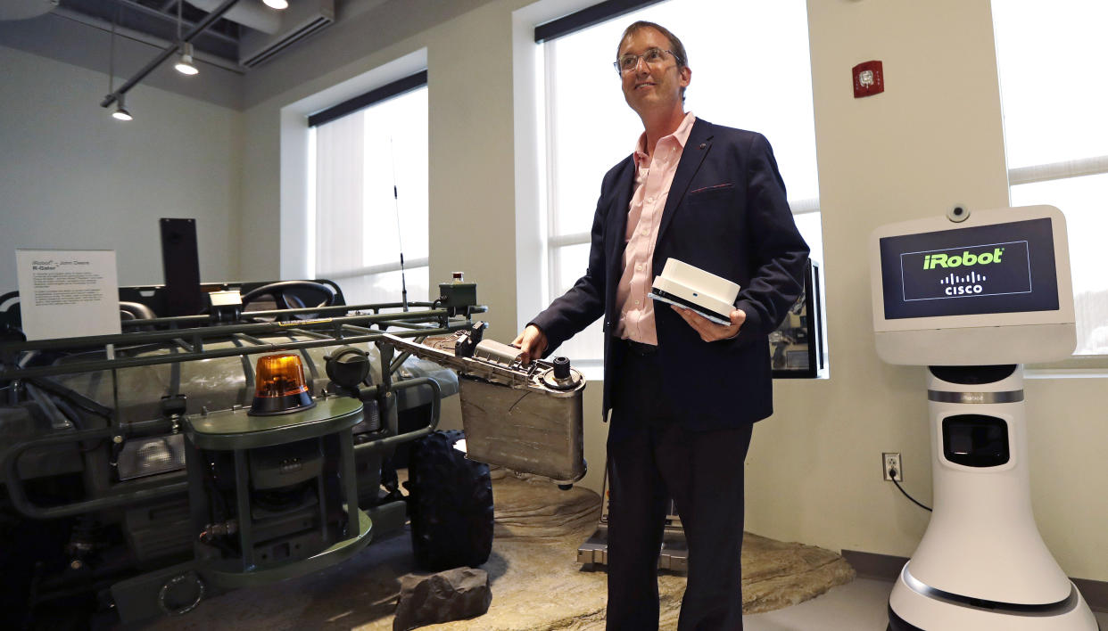 In this Thursday, Aug. 25, 2016, photo, iRobot co-founder and CEO Colin Angle holds up a Braava Jet floor cleaner and the remains of a military PackBot, which was destroyed in service with the U.S. military in Iraq, during a tour of the company's headquarters in Bedford, Mass. Angle reflected about his company's transition away from military projects to household robots during an interview with The Associated Press. (AP Photo/Charles Krupa)